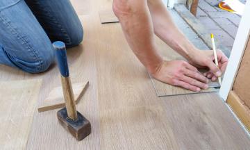 A man is marking the floor to place down wood flooring.