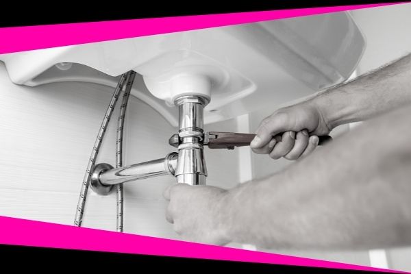 A man's hands shown holding a wrench while he his repairing the pipes on a bathroom sink.