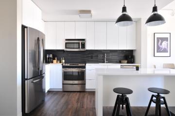 White modern kitchen with a French door fridge, white bar with black barstools, and gray brick backsplash.
